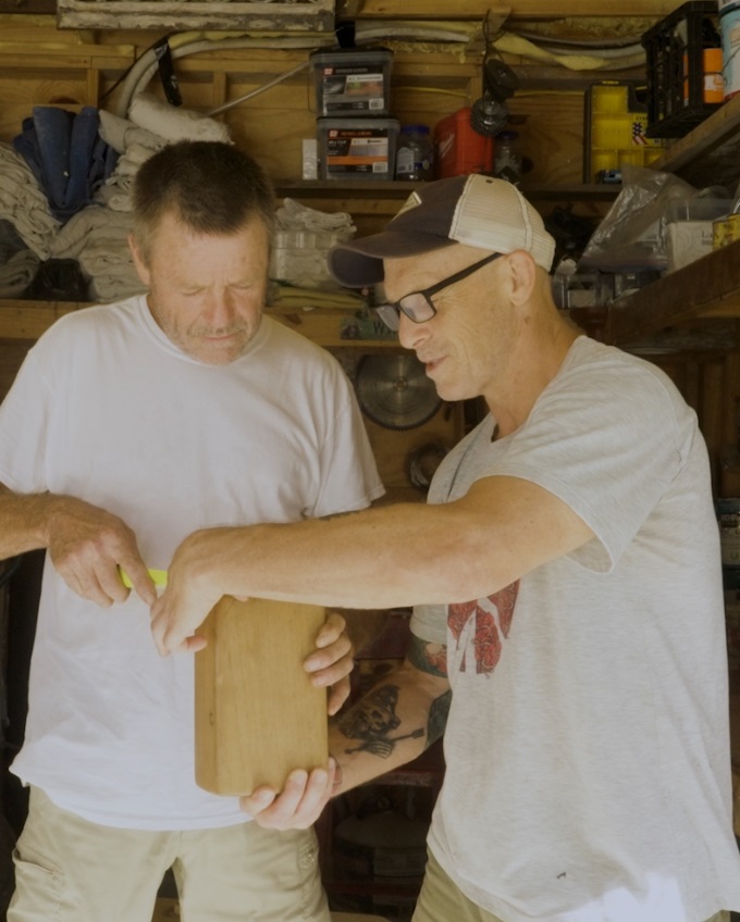 Two craftsmen in woodshop examining a handcrafted wooden block together